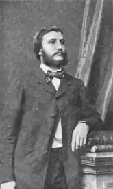 Portrait of Henri Payen, cut below the trunk. He is dressed in a suit, with a bow tie. Looking to the left, he is leaning on a pile of books.