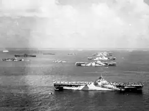 Black and white photograph of six aircraft carriers and other ships moored in rows