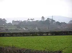 Houses amongst trees seen across fields and hedges.